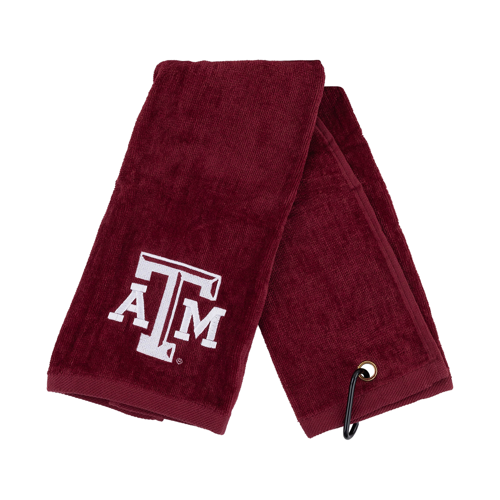 A maroon cotton golf towel featuring the white embroidered 'A&M' logo of the University of Texas, folded to show its texture and a black grommet with a cord at the corner, set against a plain white background.