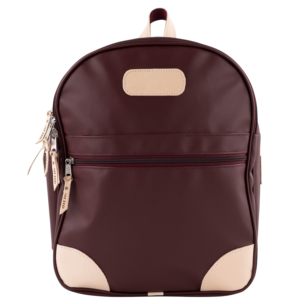 A dark burgundy backpack with beige leather-like accents on the front patch, zipper pulls, and bottom corners, shown against a plain white background.