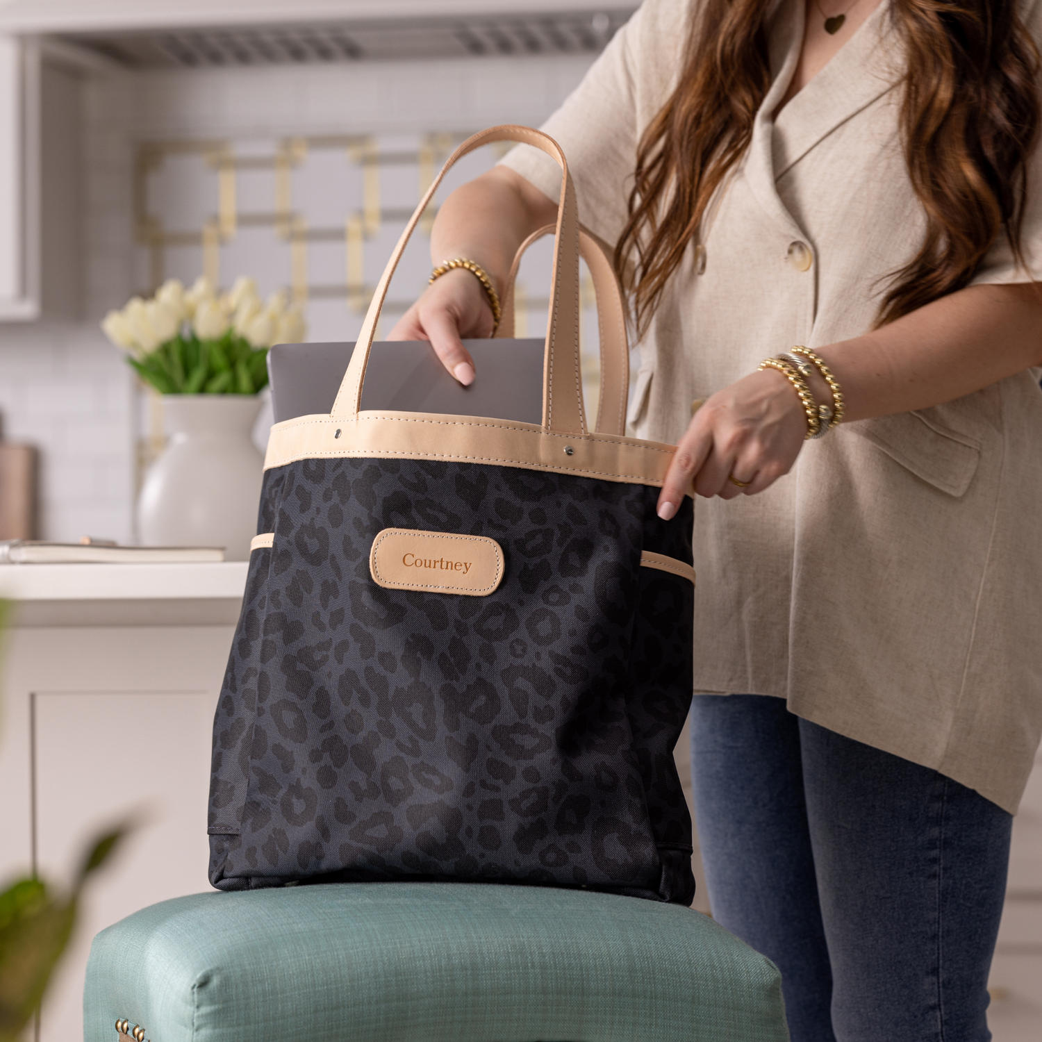 Person holding a black patterned tote bag with a visible brand logo in an indoor setting.