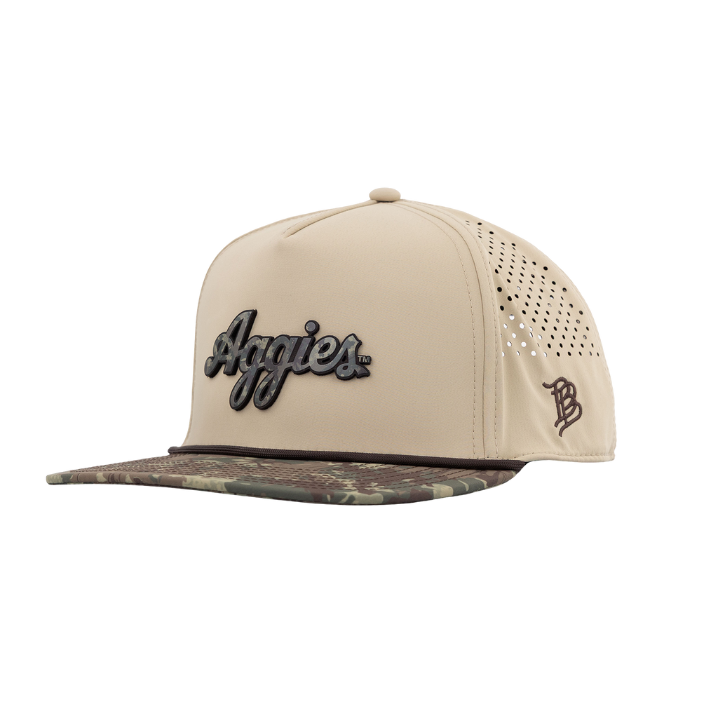 A beige snapback cap with a camouflage-patterned visor, featuring a black and gray 'Aggies' script logo on the front and a brown monogram logo on the side.