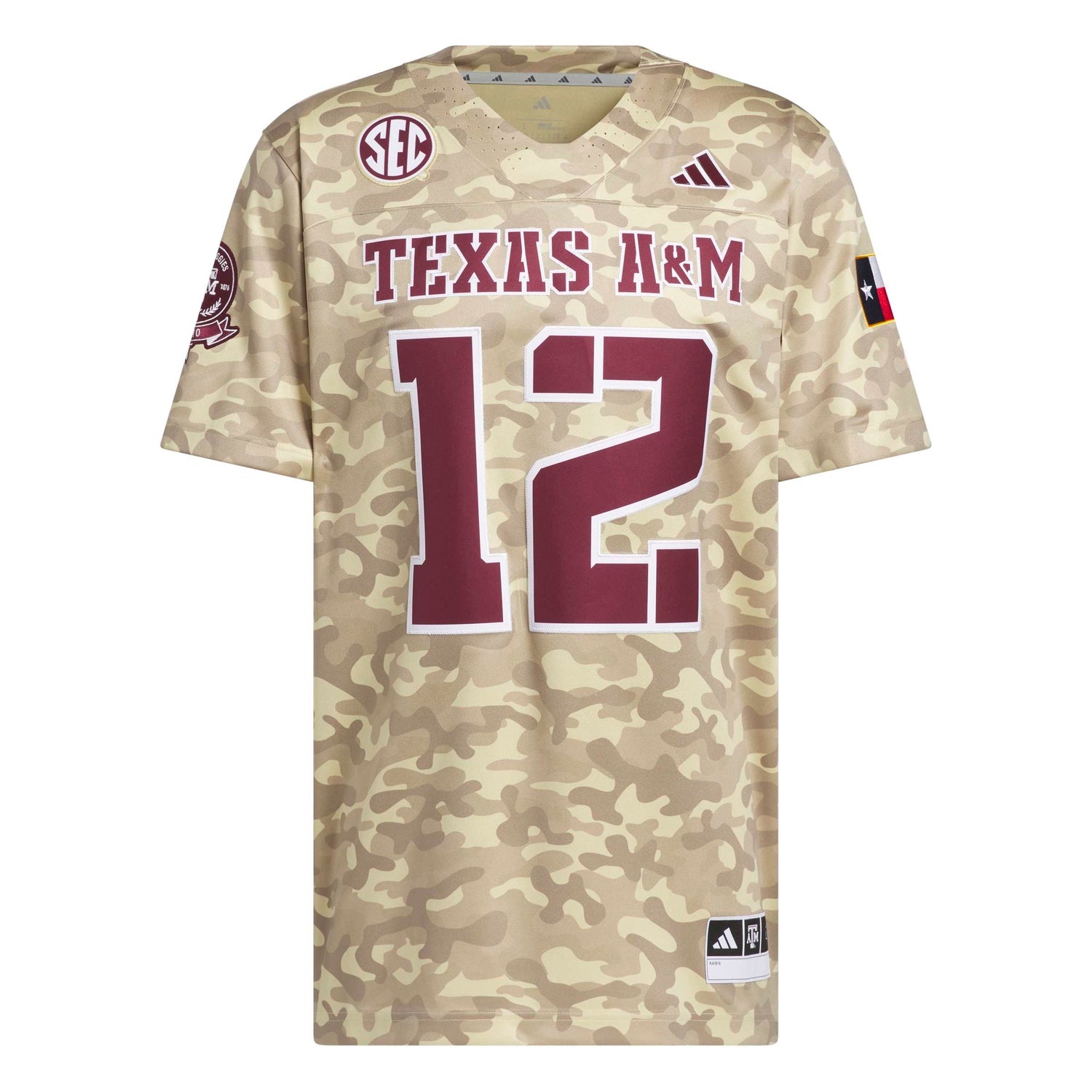 A Texas A&M football jersey in a beige and tan camouflage pattern, featuring maroon 'TEXAS A&M' lettering and the number '12' outlined in white on the front. The jersey includes the SEC logo on the left chest, an Adidas logo on the right chest, and a Texas state flag patch on the sleeve.