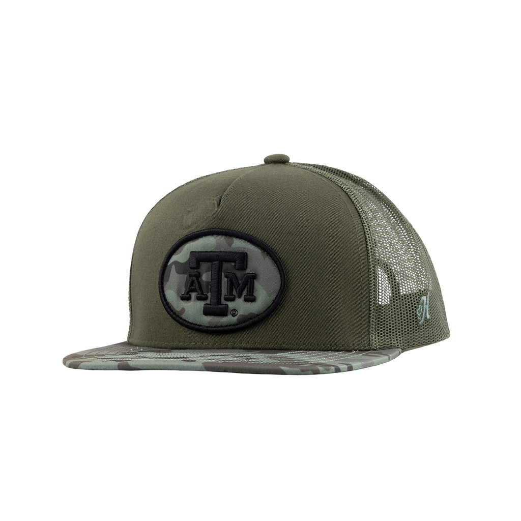 An olive green trucker hat with a camouflage-patterned brim and mesh back, featuring a black and camouflage oval patch with the Texas A&M 'A&M' logo on the front.