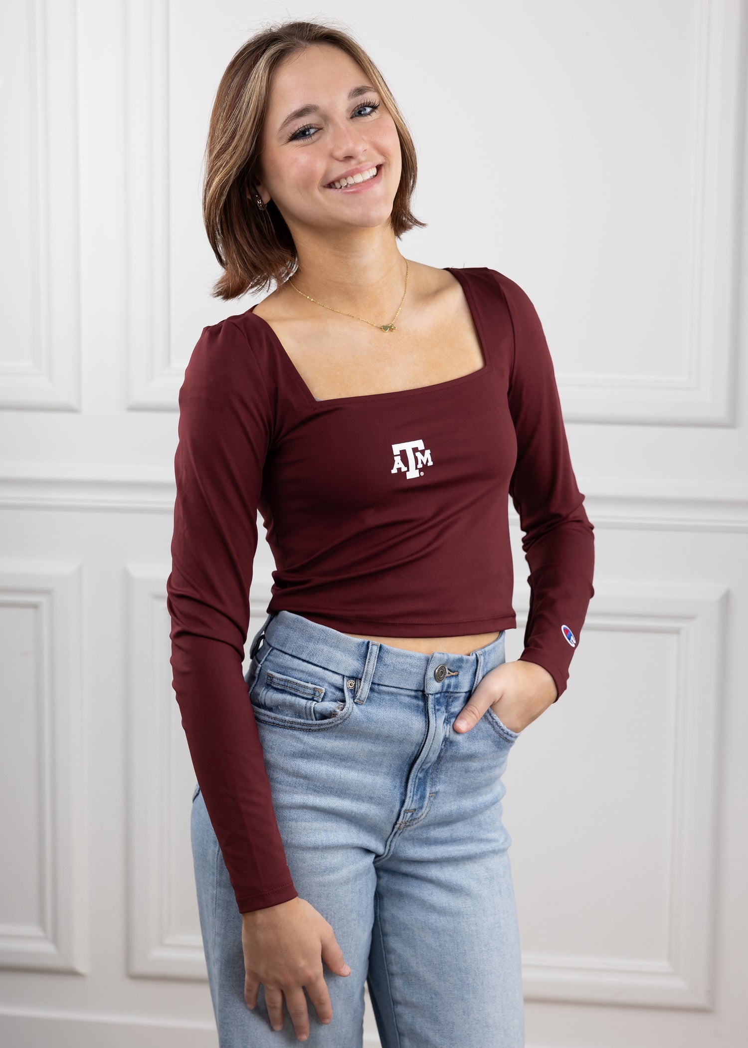 Woman wearing a maroon long-sleeve top with the Texas A&M logo in the center of the top in white.