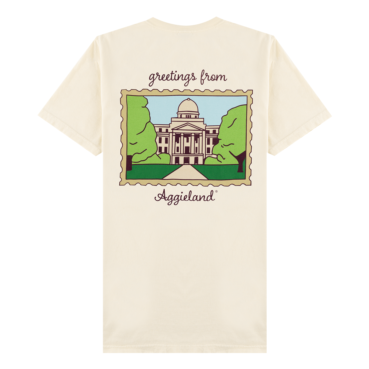 A cream-colored short-sleeve t-shirt shown from the back, featuring a graphic print of a building with a dome framed by green trees, with the text 'greetings from Aggieland' written above and below the illustration.