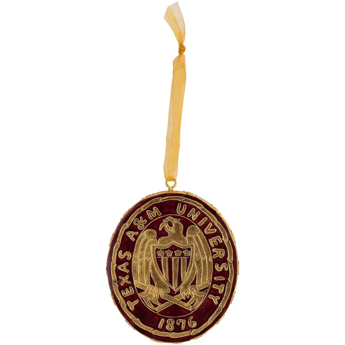 A circular Texas A&M University ornament featuring a gold crest and lettering on a dark burgundy background, suspended by a sheer gold ribbon against a plain white background.