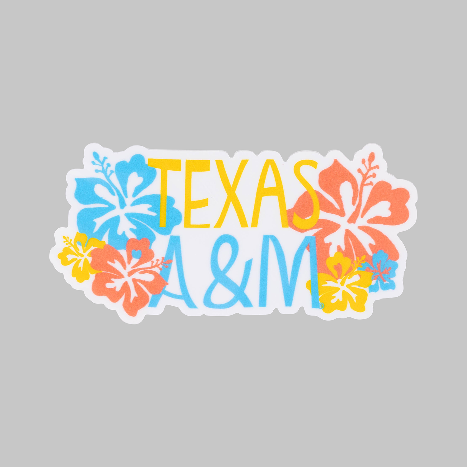 A die-cut sticker featuring the text 'TEXAS A&M' in yellow and light blue, surrounded by colorful hibiscus flowers in orange, yellow, and blue, shown on a solid gray background.