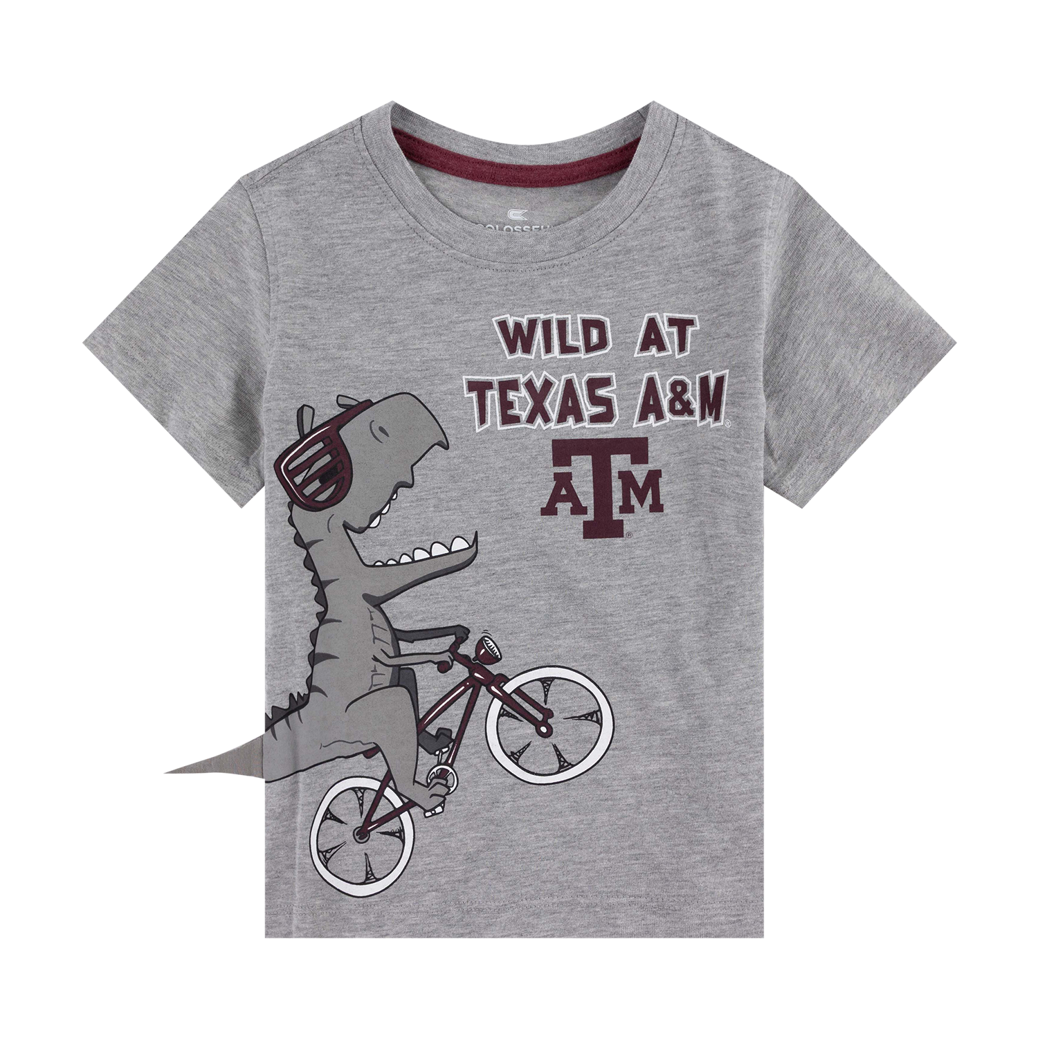 A toddler's heather gray short-sleeve t-shirt featuring a cartoon dinosaur wearing sunglasses and riding a bicycle, with the text 'WILD AT TEXAS A&M' and 'A&M' logo printed on the front.